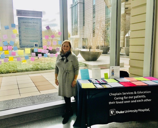 Sue Ann Glower stands with Chaplin Services table at Grief Awareness Week 